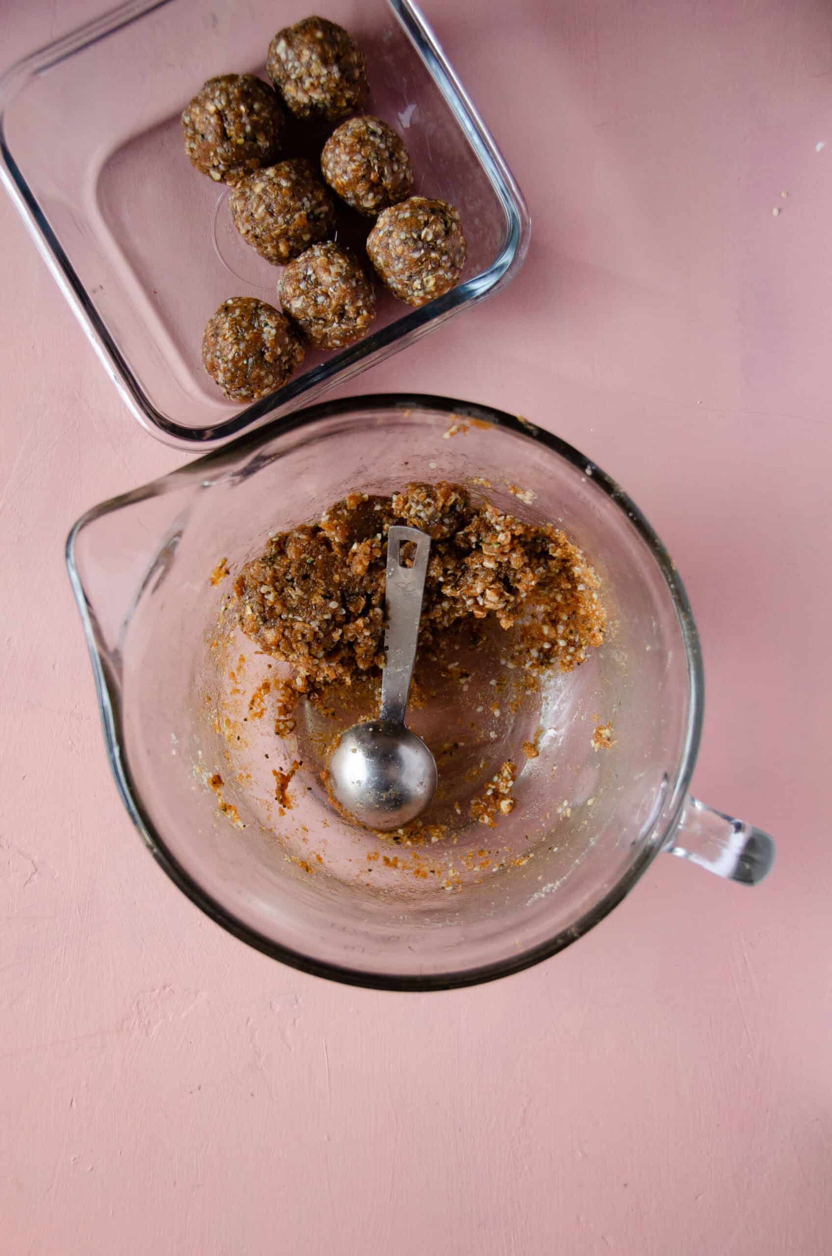 A glass mixing bowl with energy ball dough being scooped with a tablespoon into energy balls.
