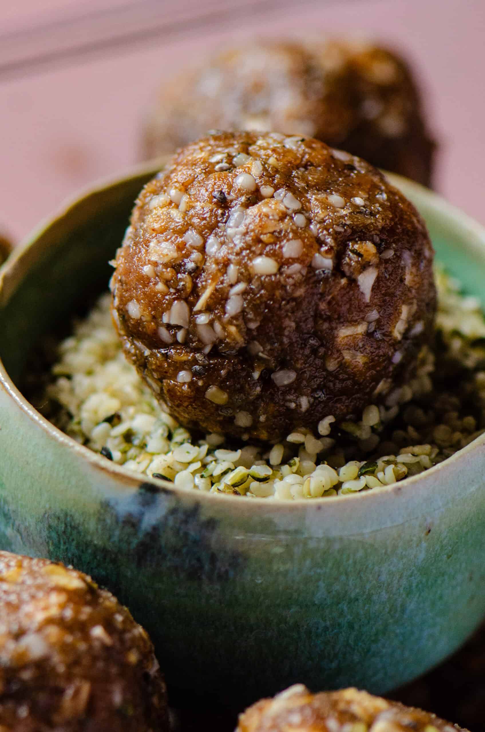 A brown energy balls sitting in a small bowl filled with hemp hearts.
