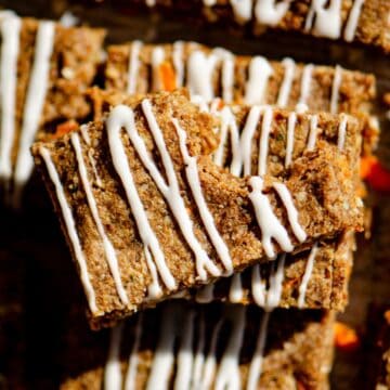 Brown carrot protein bar with a bite out of it drizzled with white cream cheese glaze all cut into rectangles.