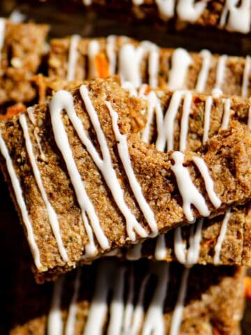 Brown carrot protein bar with a bite out of it drizzled with white cream cheese glaze all cut into rectangles.