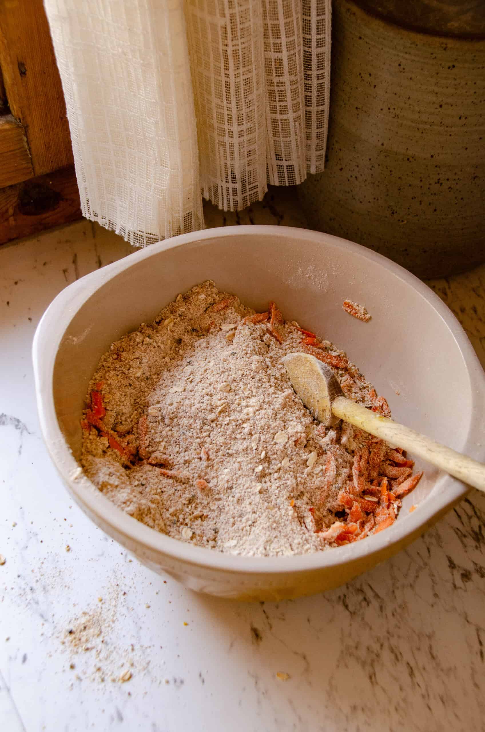 Shredded carrots being folded into a bowl of dry ingredients.