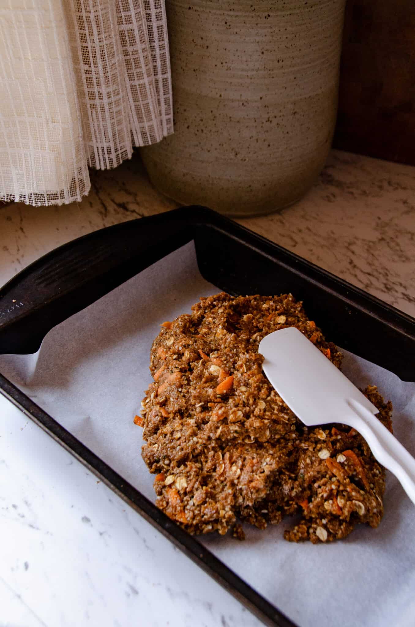 Spreading thick dough into a rectangular pan with a white spatula.