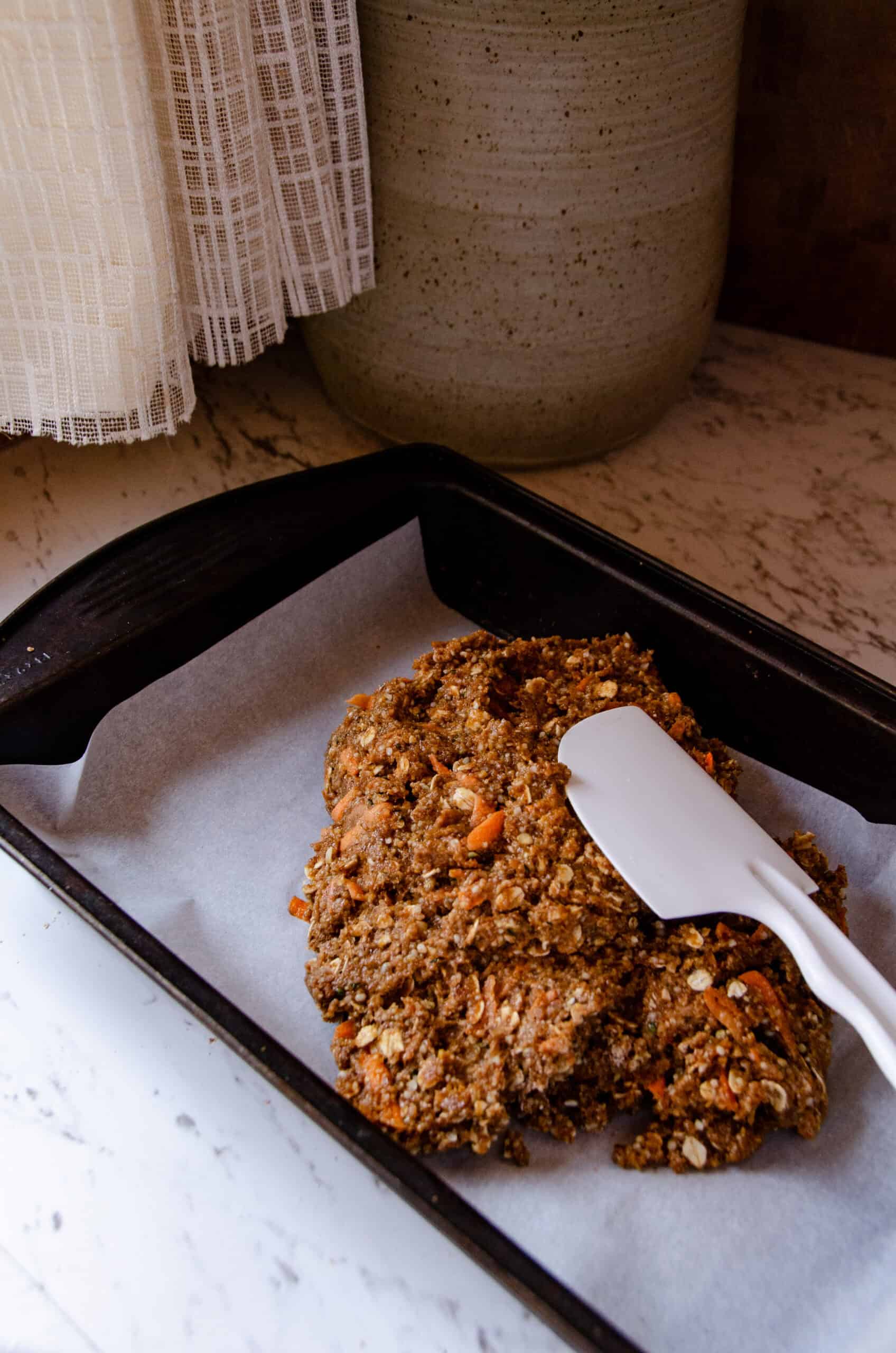Spreading thick dough into a rectangular pan with a white spatula.