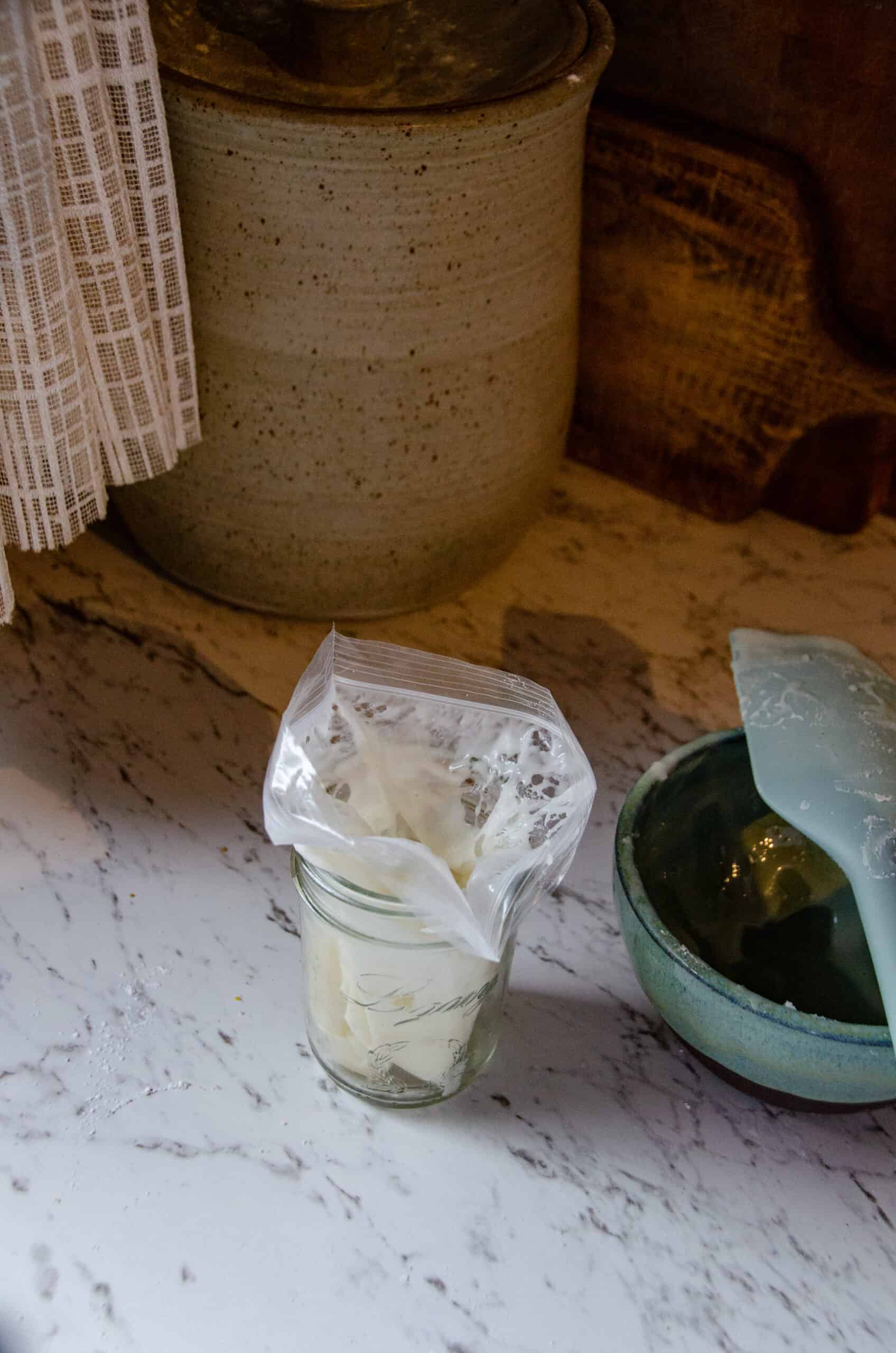Cream cheese icing being placed in a ziplock bag after being mixed in a bowl with a spatula that is beside it.
