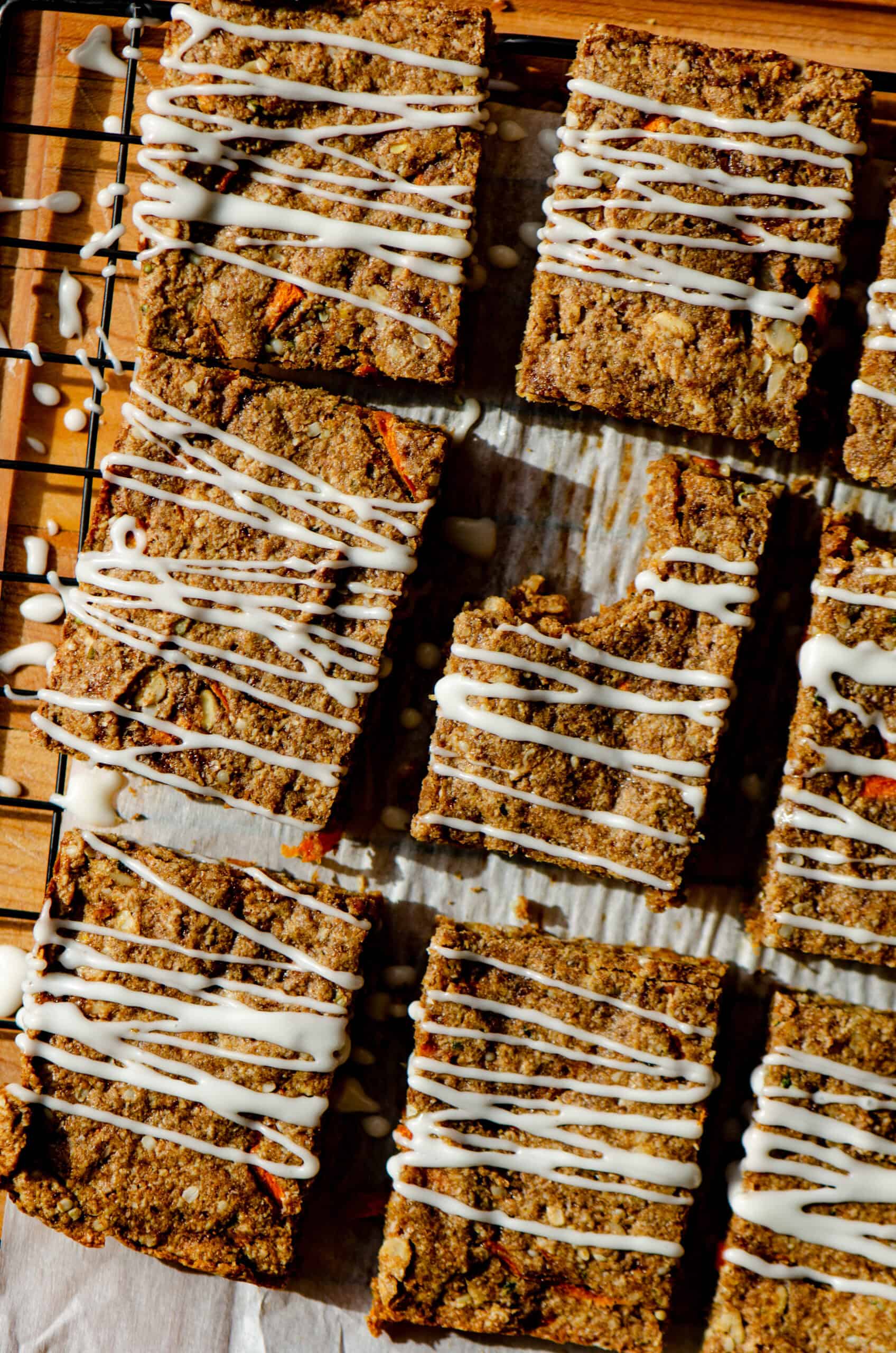 Brown carrot protein bars drizzled with white cream cheese glaze all cut into rectangles.