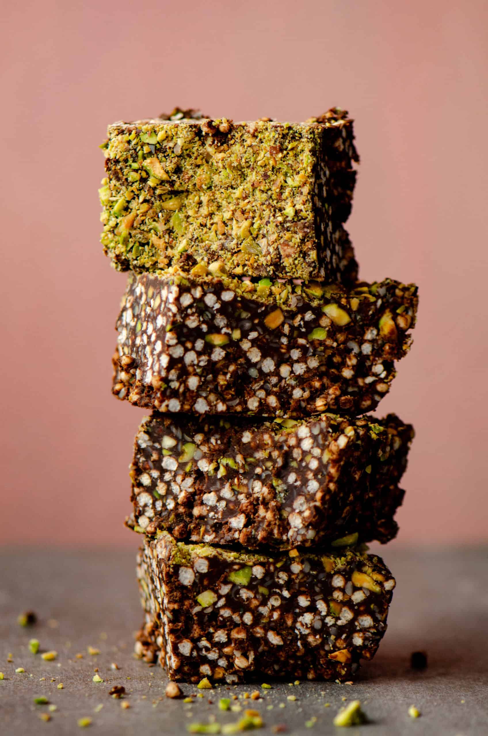 Puffed quinoa chocolate squares stacked with green chopped pistachios on top.