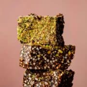 Puffed quinoa chocolate squares stacked with green chopped pistachios on top.