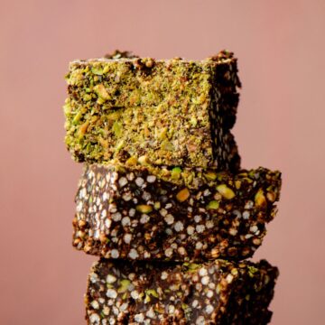 Puffed quinoa chocolate squares stacked with green chopped pistachios on top.