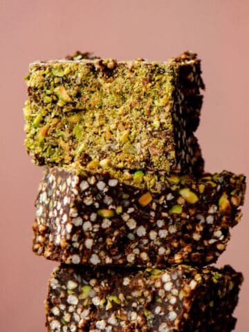Puffed quinoa chocolate squares stacked with green chopped pistachios on top.