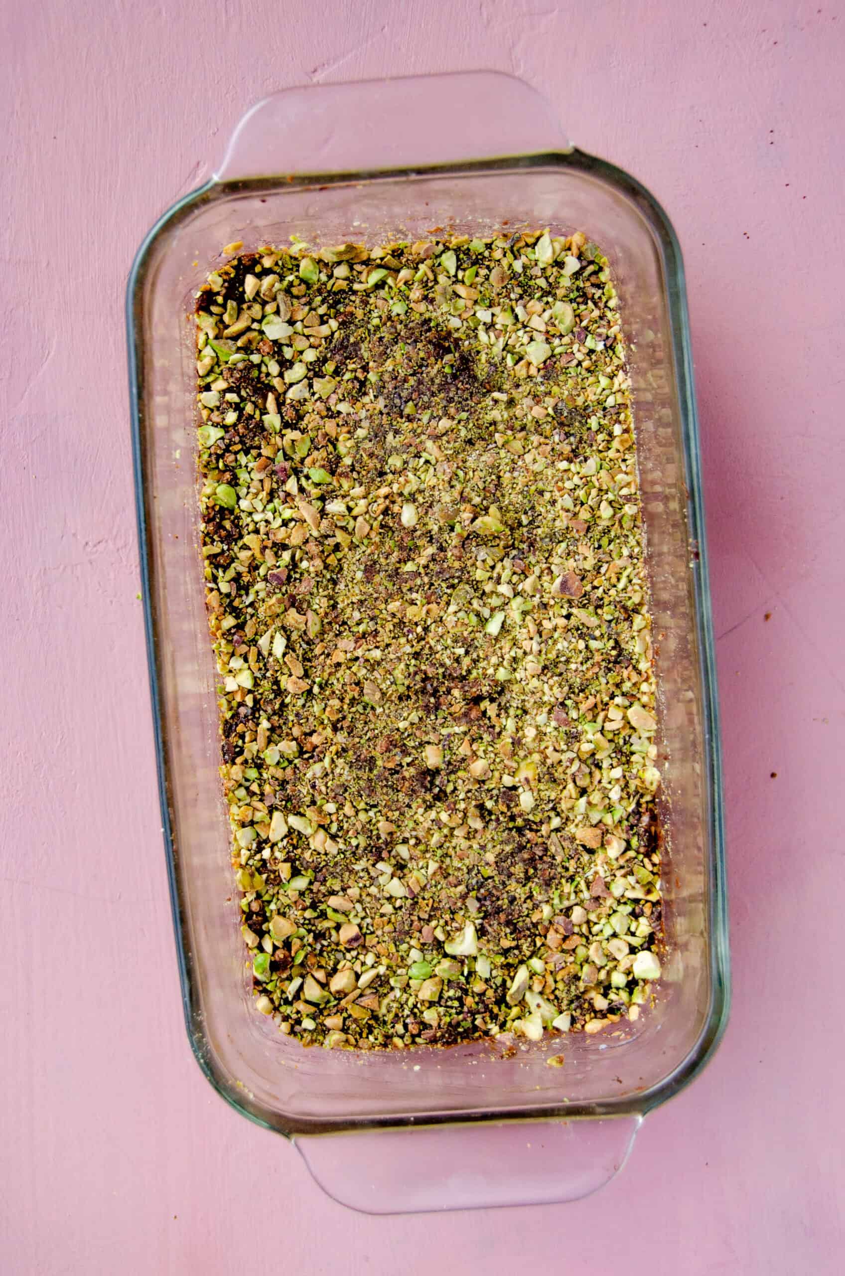 A loaf pan with chocolate puffed quinoa bars with pistachios on top.