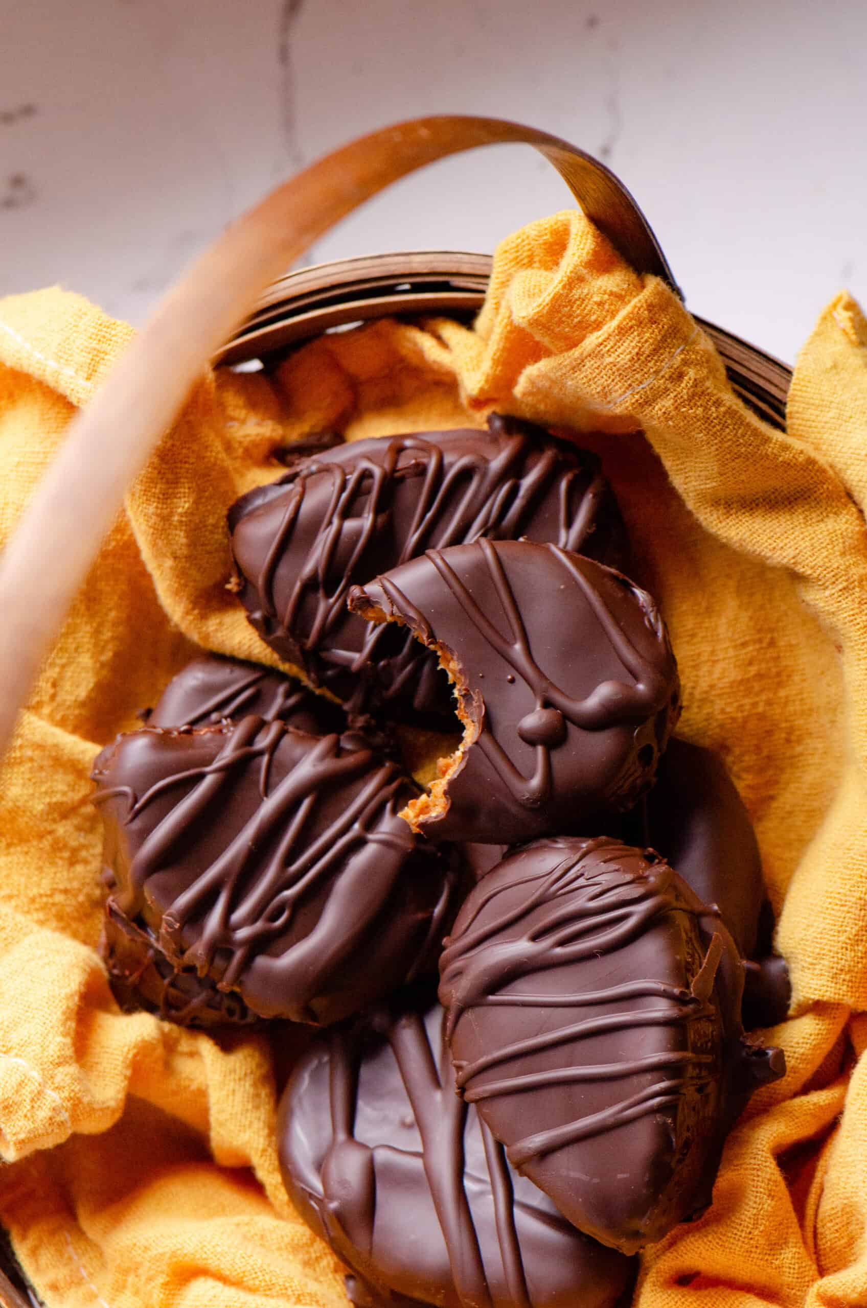 Chocolate easter eggs with a bite taken of of one showing an orange middle, in a straw easter basket.