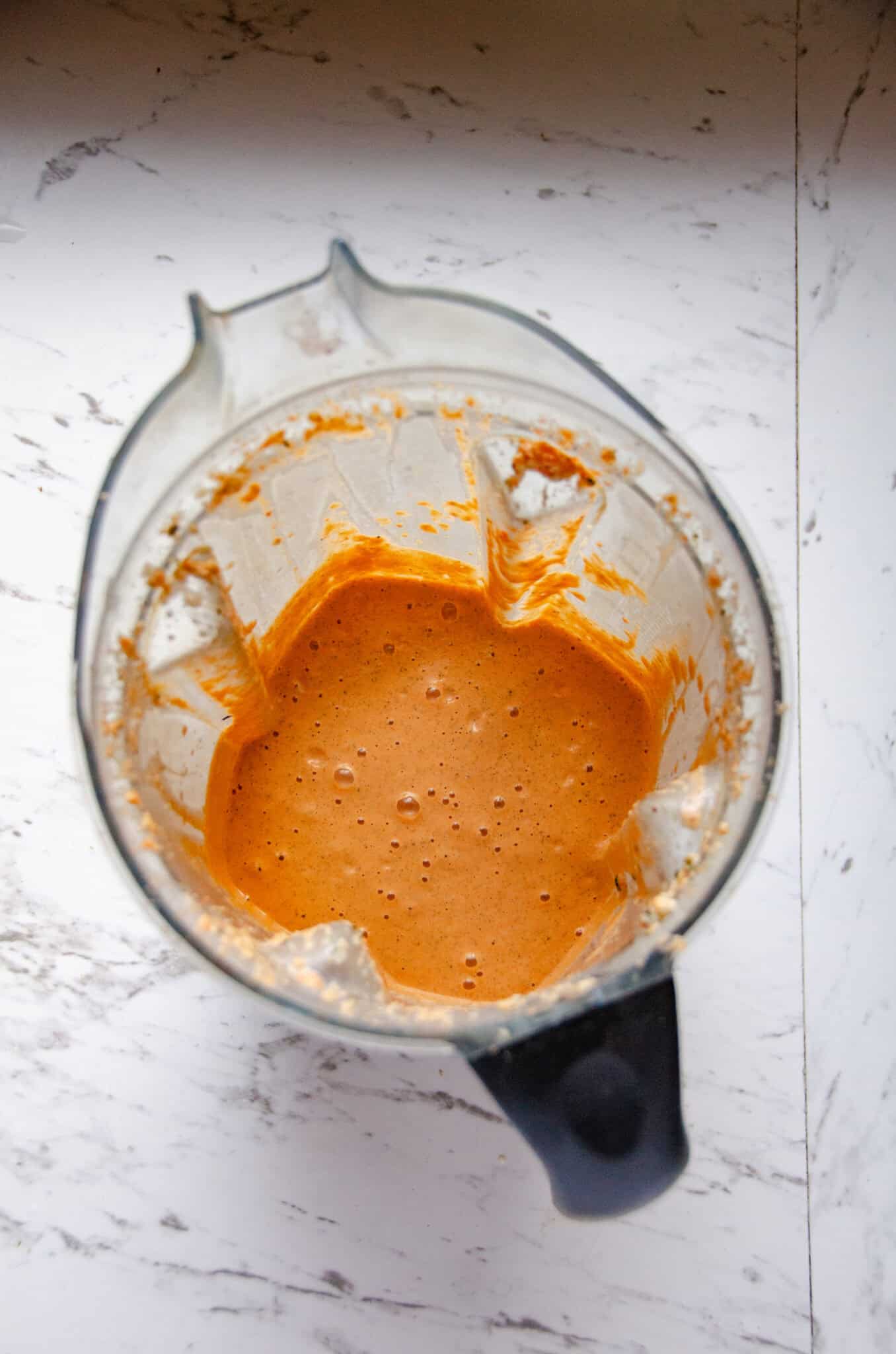An orange colored red pepper dip in a blender container.