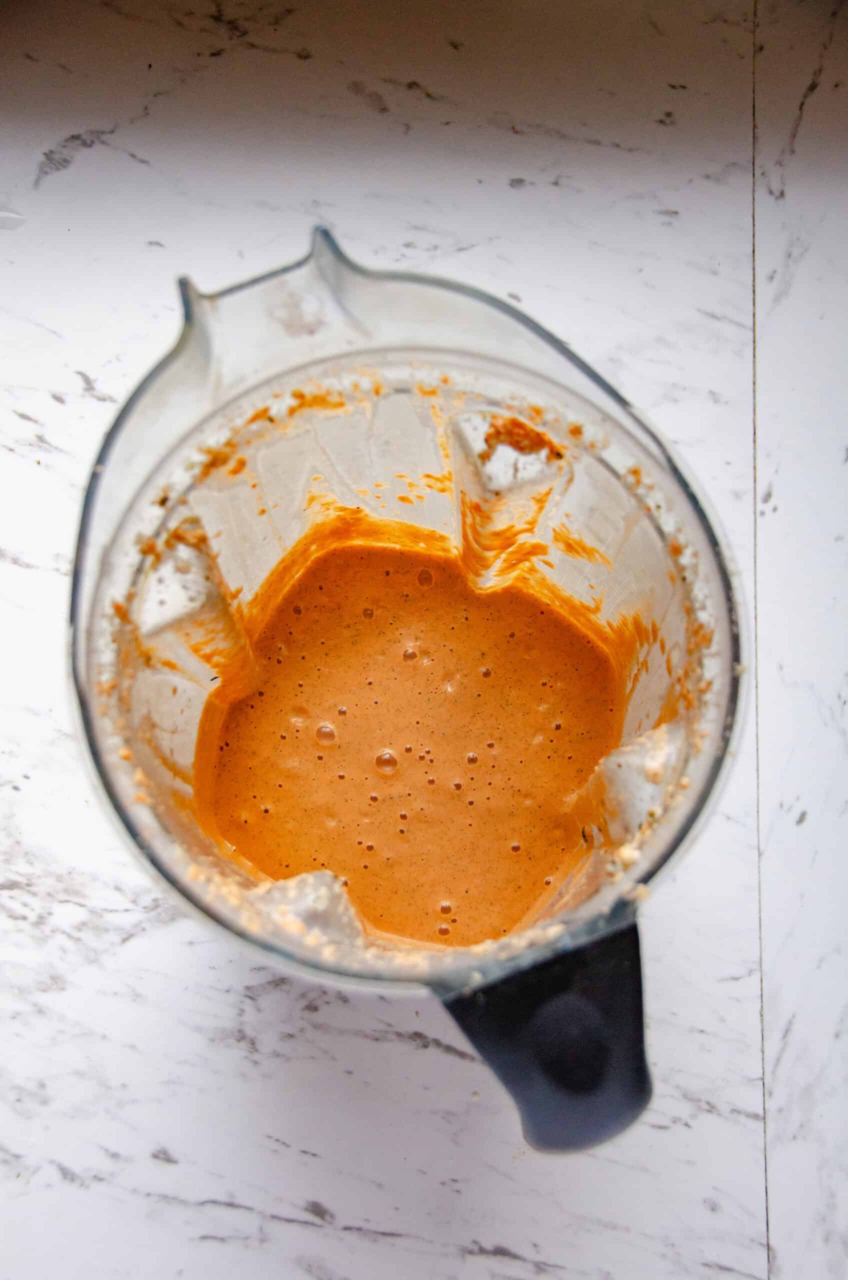 An orange colored red pepper dip in a blender container.