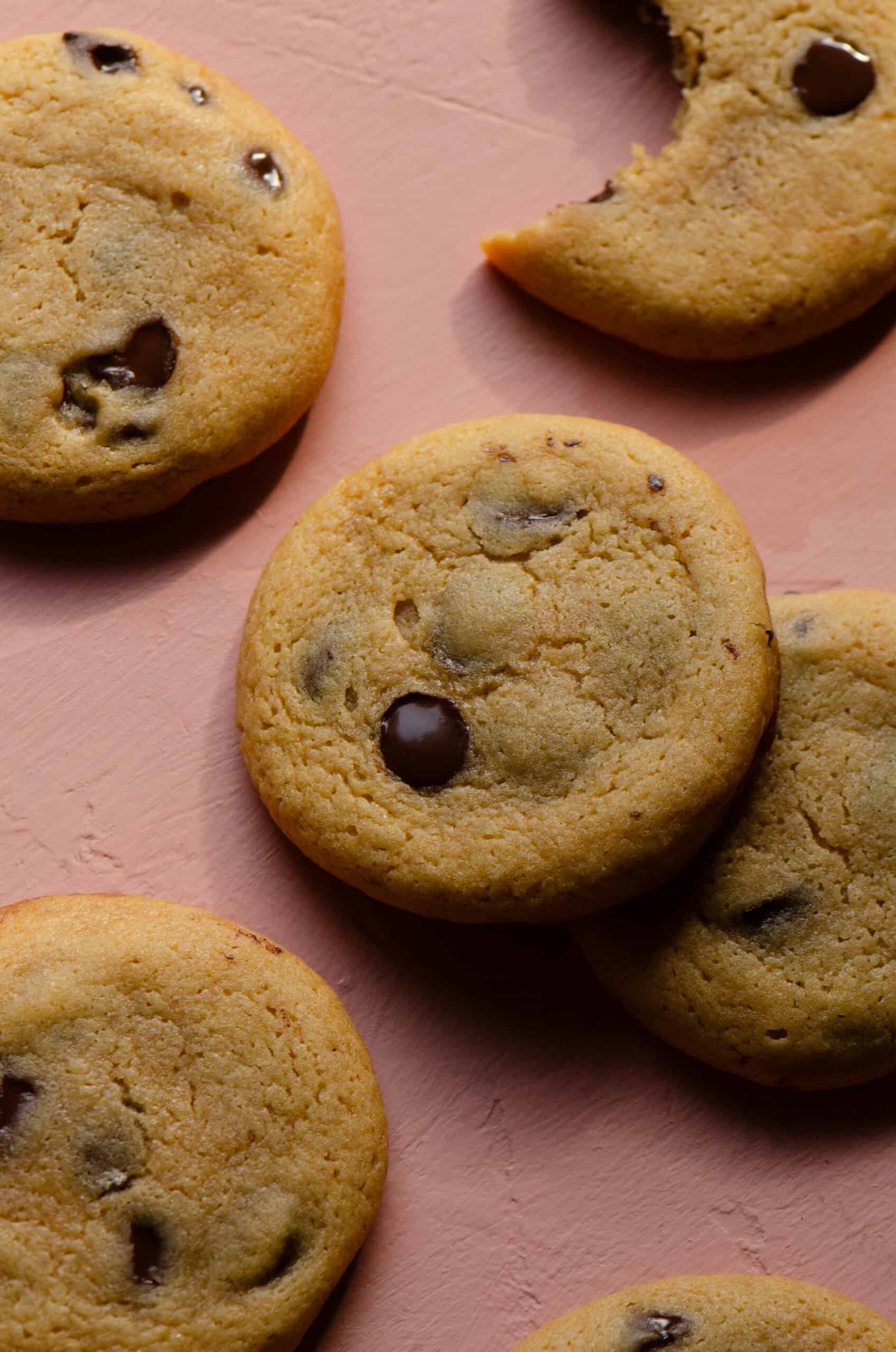 Honey chocolate chip cookies on a pink counter, one with a bite missing.
