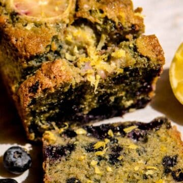 A loaf of lemon blueberry bread with blueberries and lemon beside it.