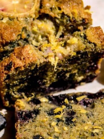A loaf of lemon blueberry bread with blueberries and lemon beside it.