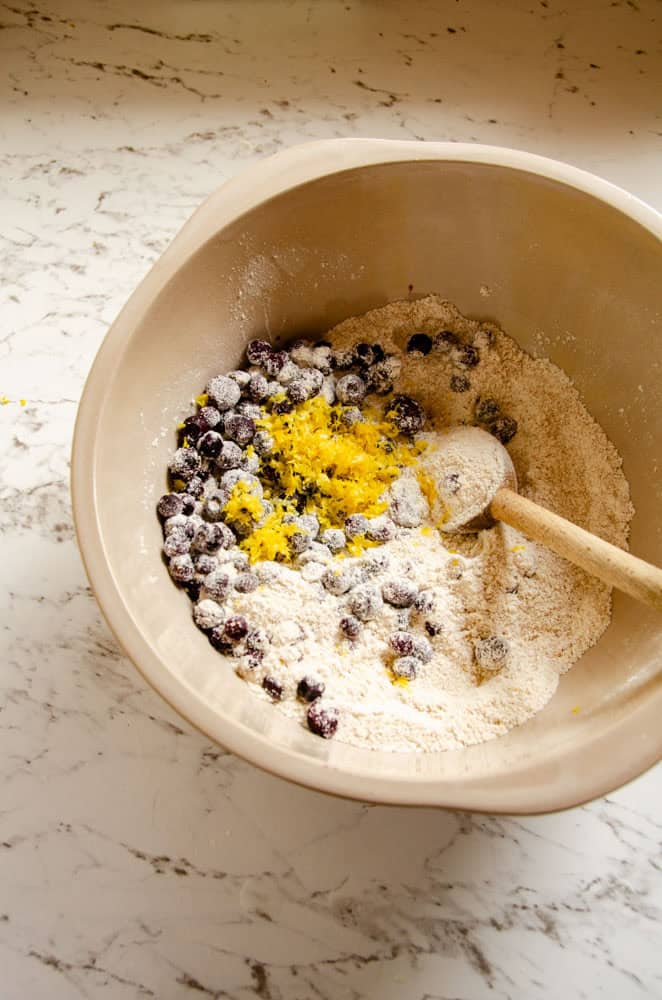 A bowl with dry ingredients, lemon zest and blueberries.