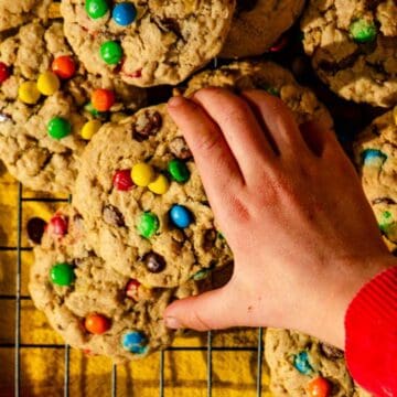 A small hand grabbing a cookie with colorful candies on the cookie.