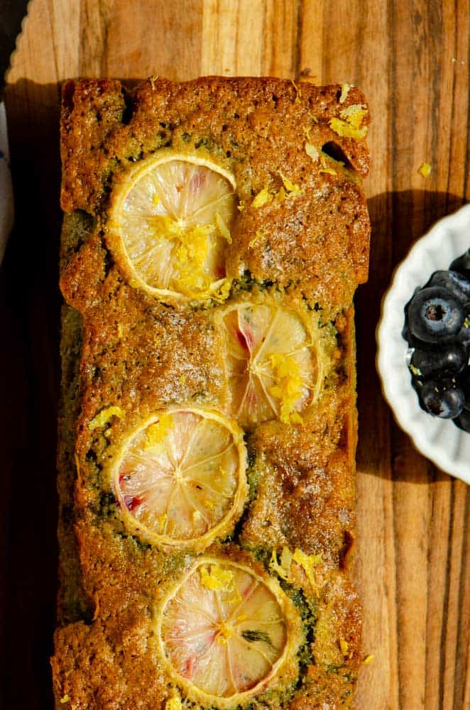 A pretty loaf with lemon sliced baked onto the top. with a bowl of the blueberries beside it. 