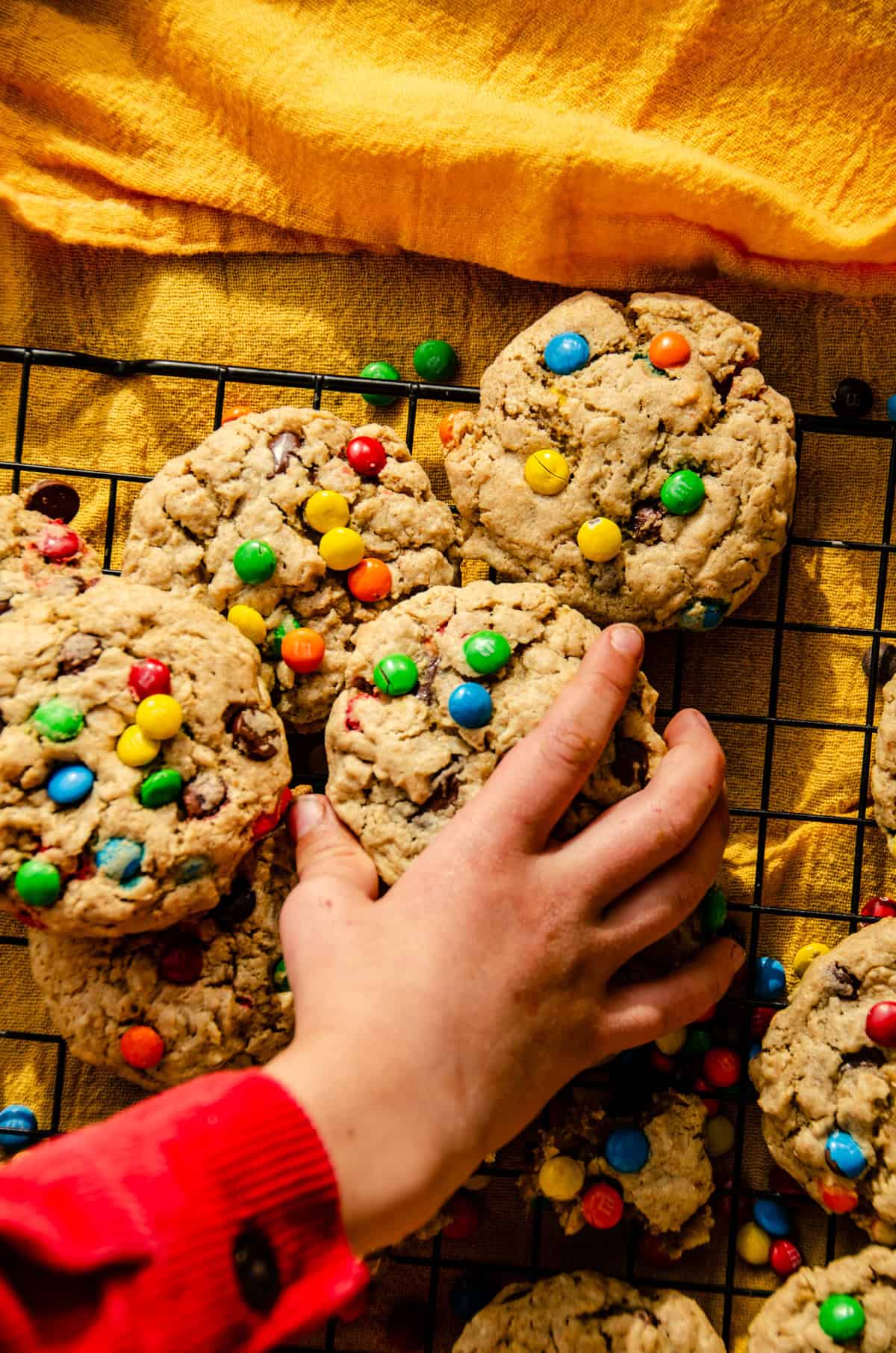 A small hand grabbing a cookie with colorful candies on the cookie.