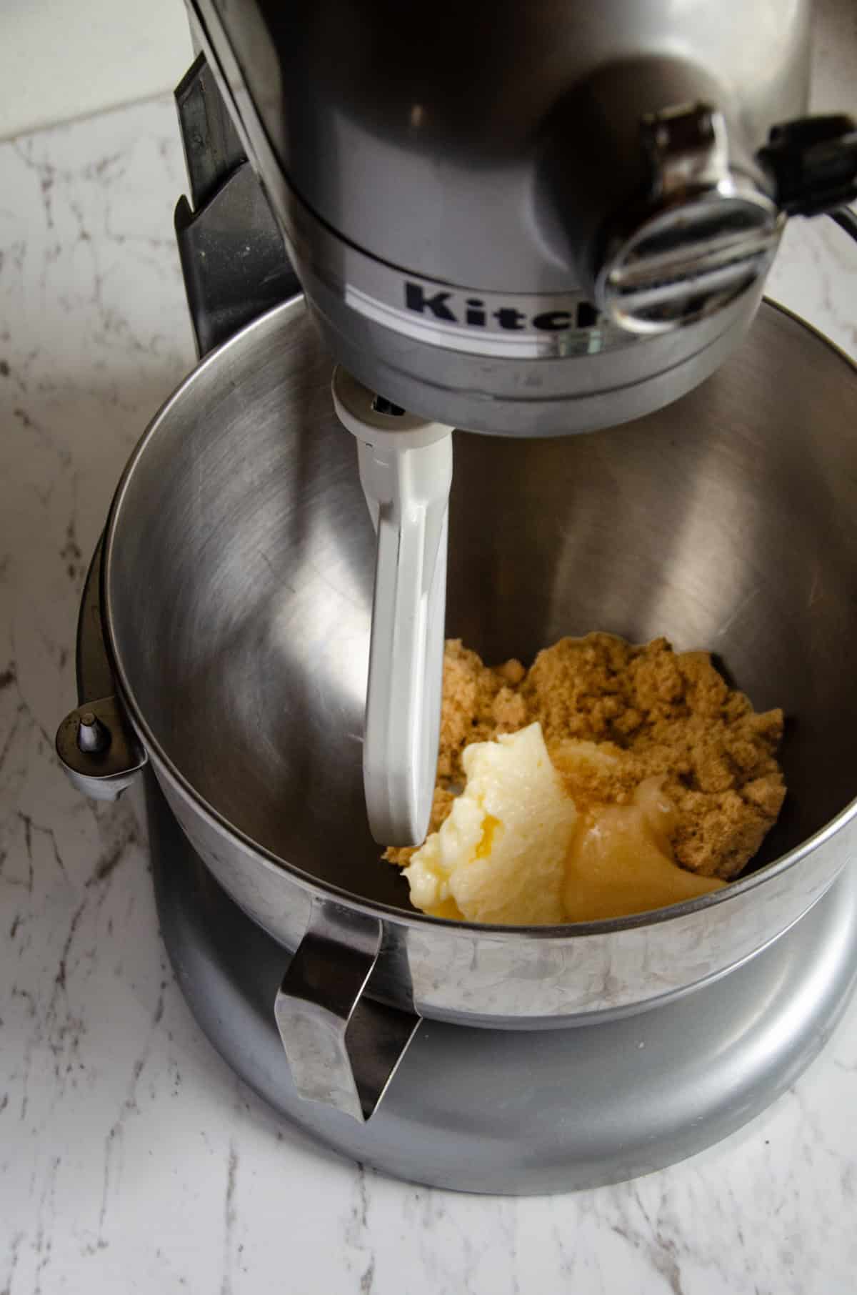 A mixer with butter and brown sugar in it.