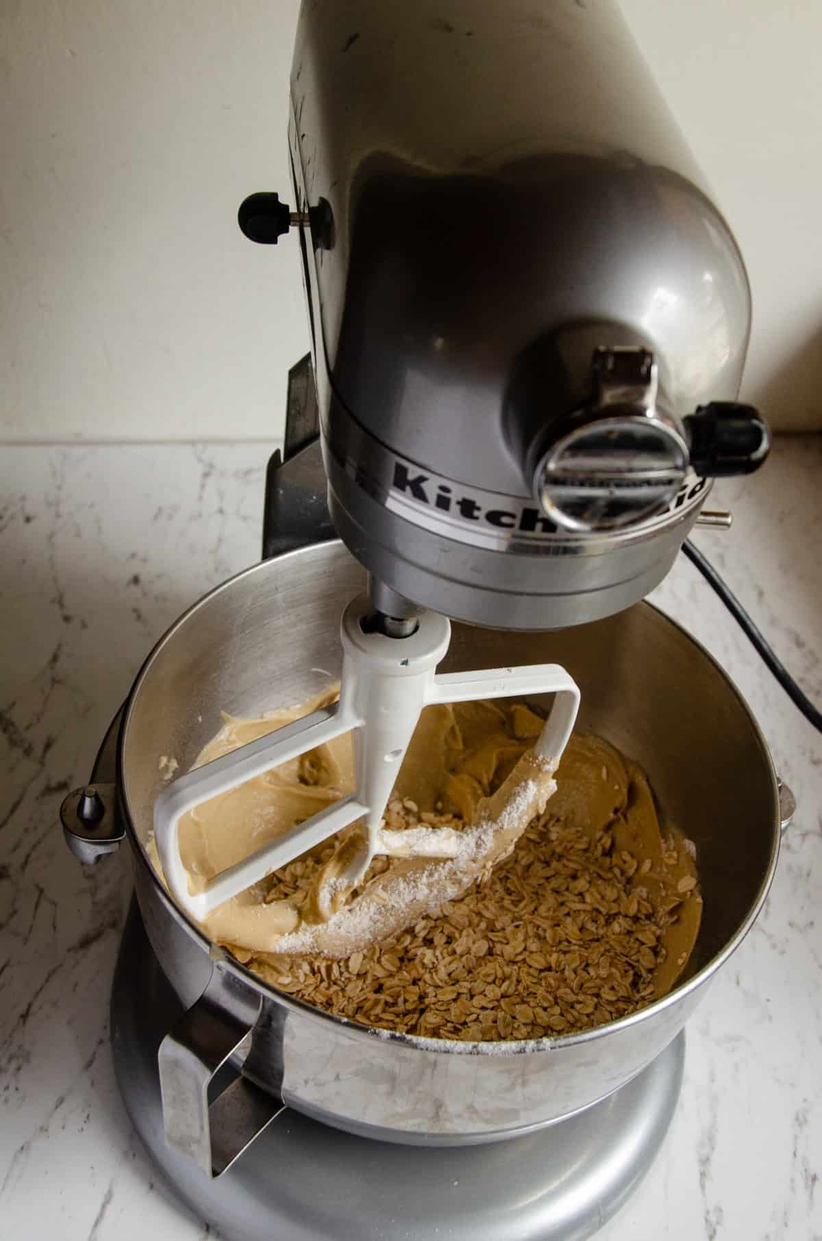 Rolled oats added to cookie batter in a mixer bowl.