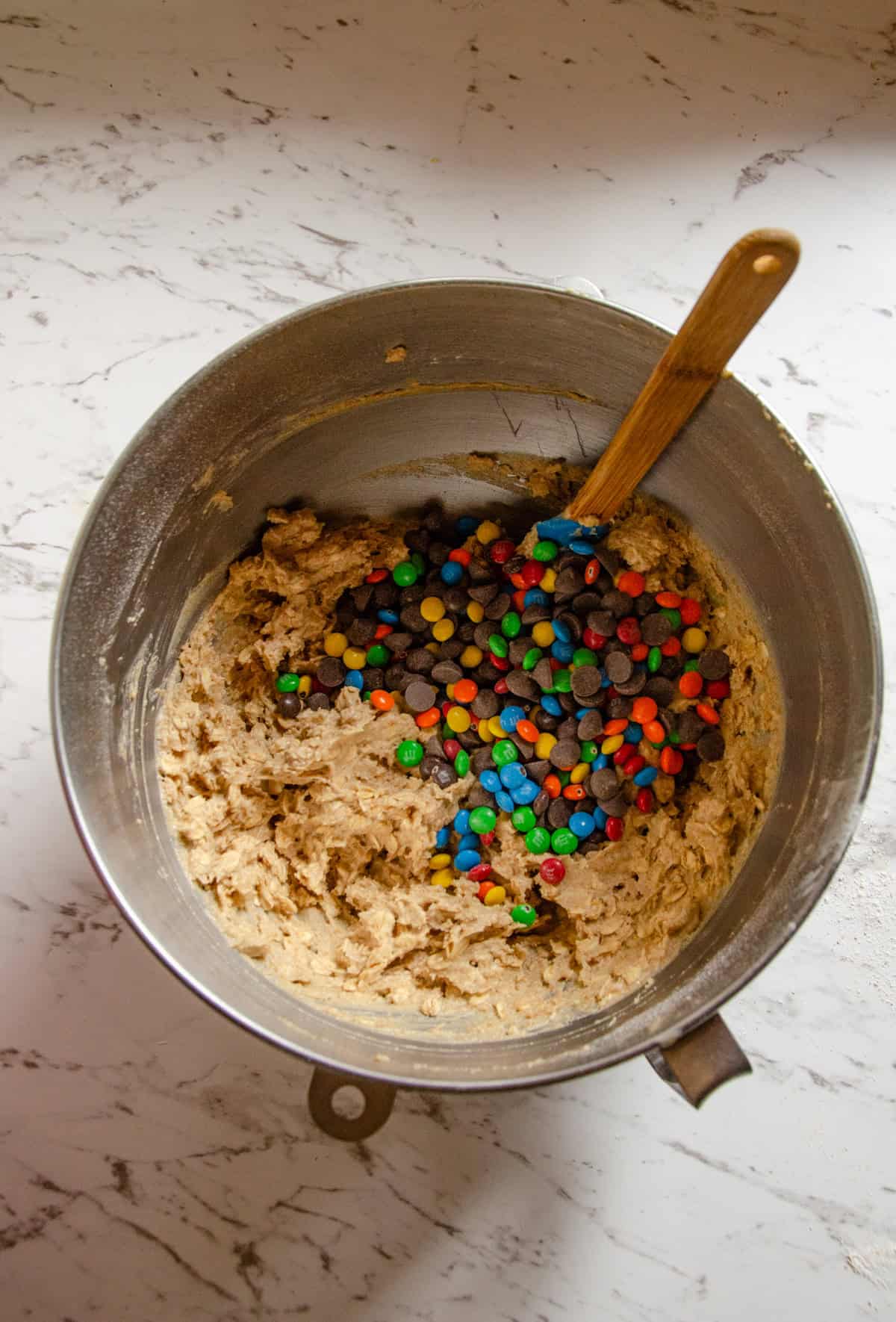 Colorful candies being added to cookie dough in a bowl with a spatula in the bowl.