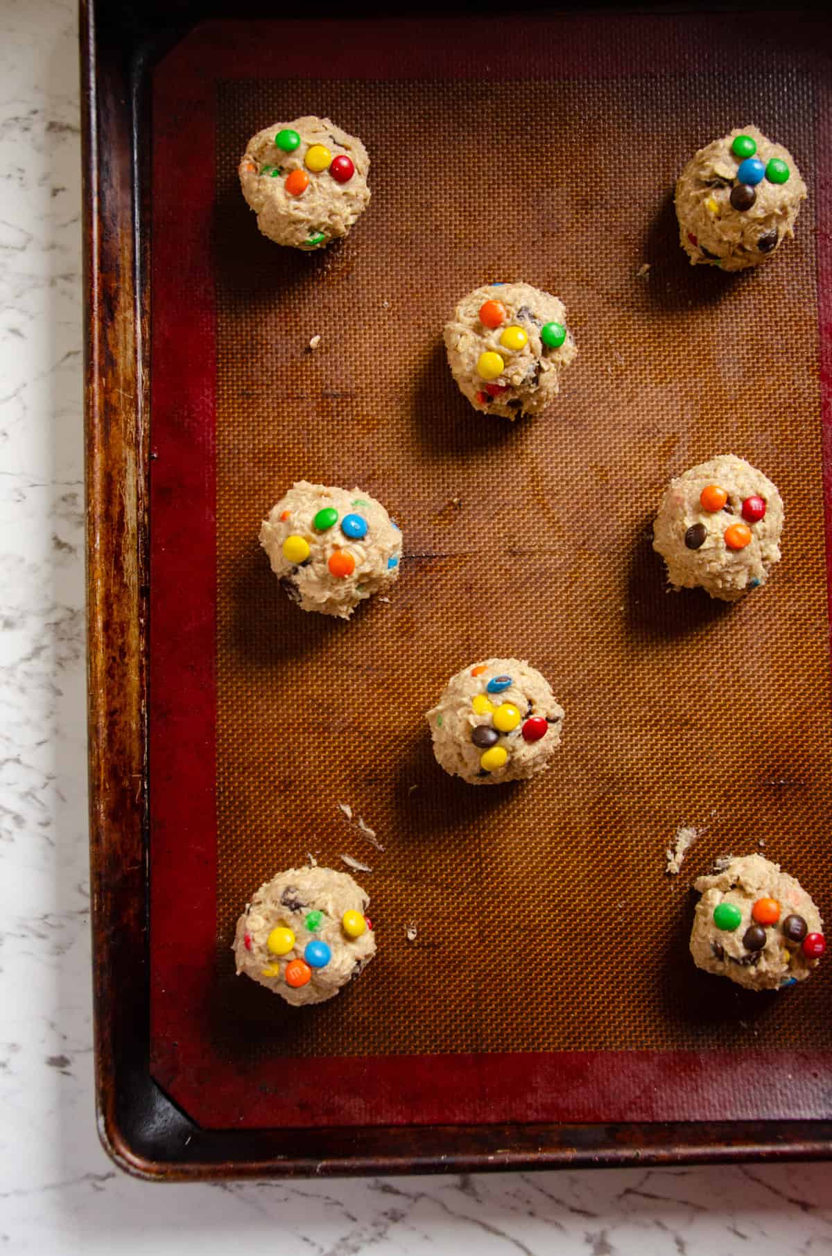 Cookie dough balls on a cookie sheet with colorful candies on top.