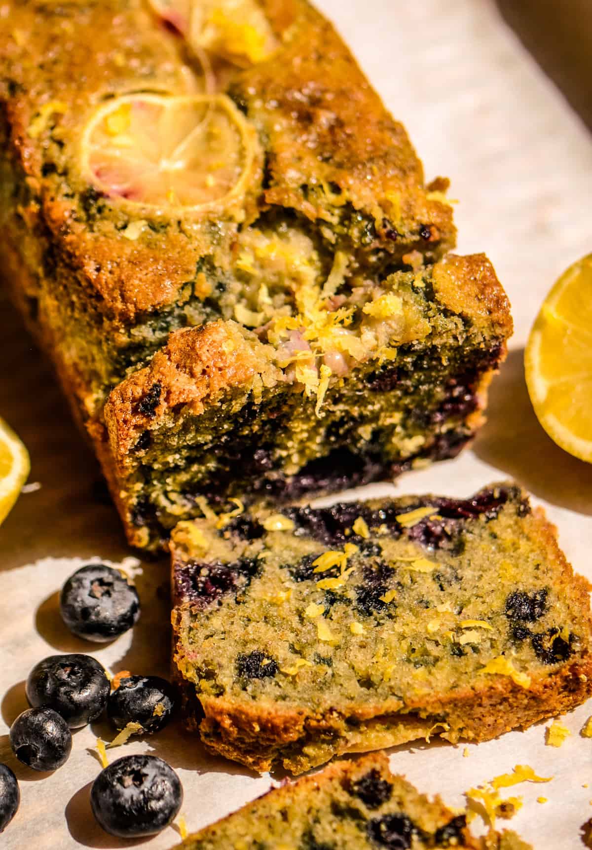 A loaf of lemon blueberry bread with blueberries and lemon beside it.
