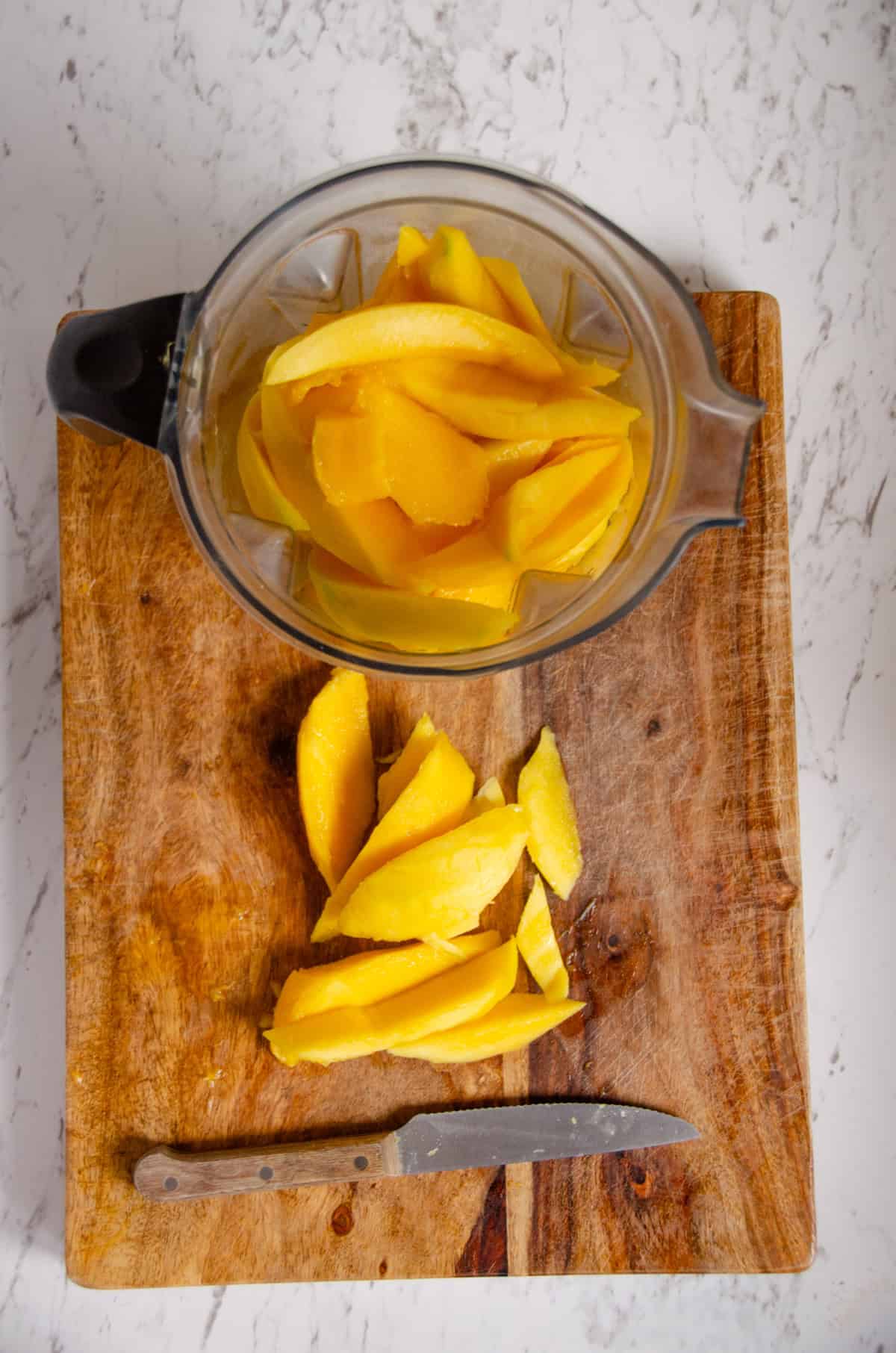 A blender container with pieces of mango in it.