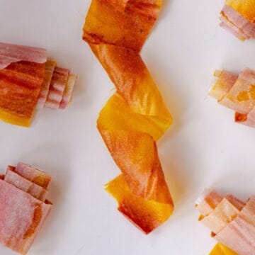 A pink and yellow fruit roll up twisted with other fruit roll ups on parchment paper beside it.