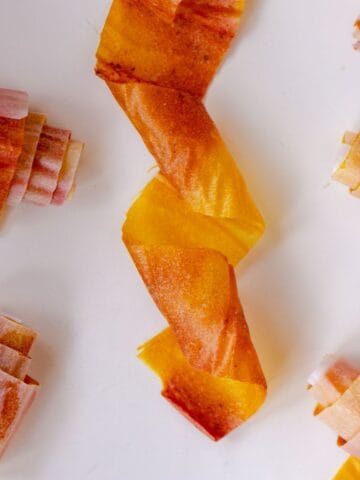 A pink and yellow fruit roll up twisted with other fruit roll ups on parchment paper beside it.