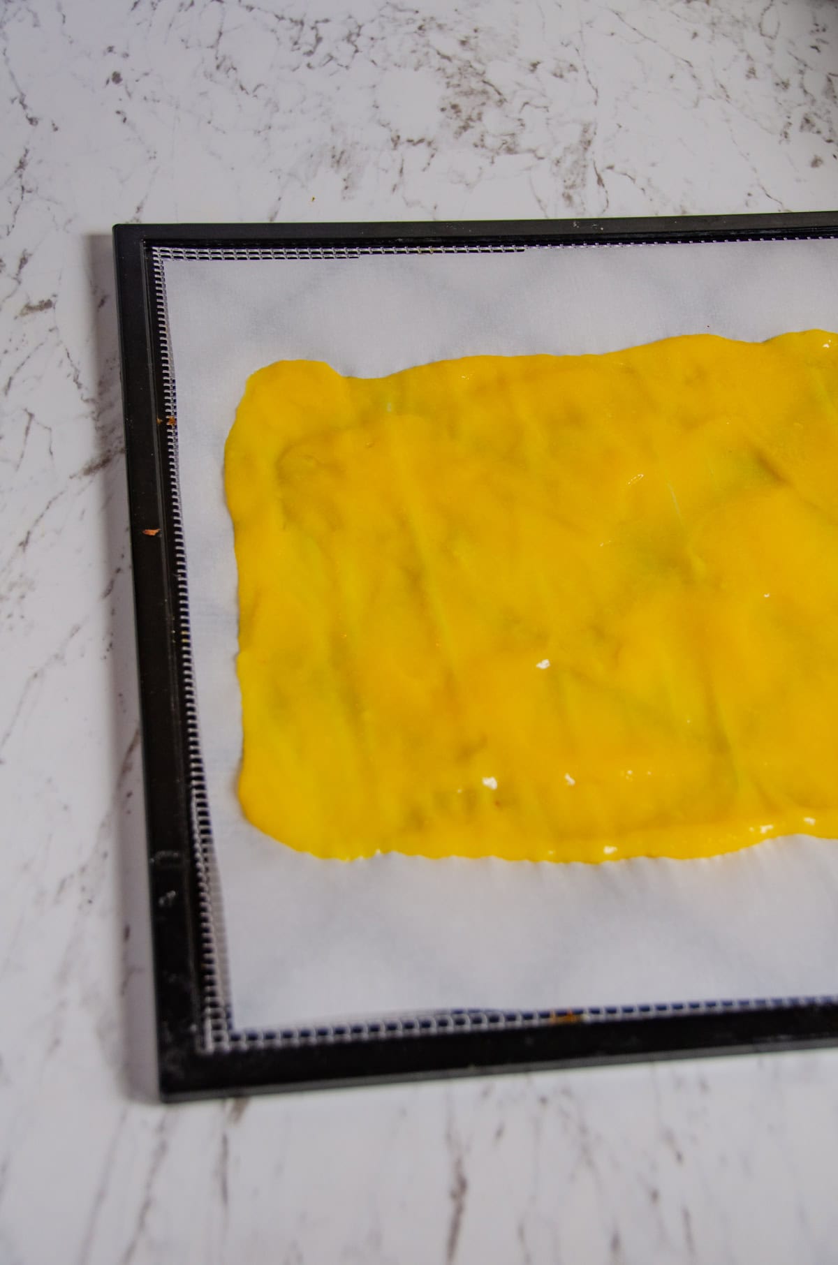 Yellow mango puree spreading out on parchment paper.