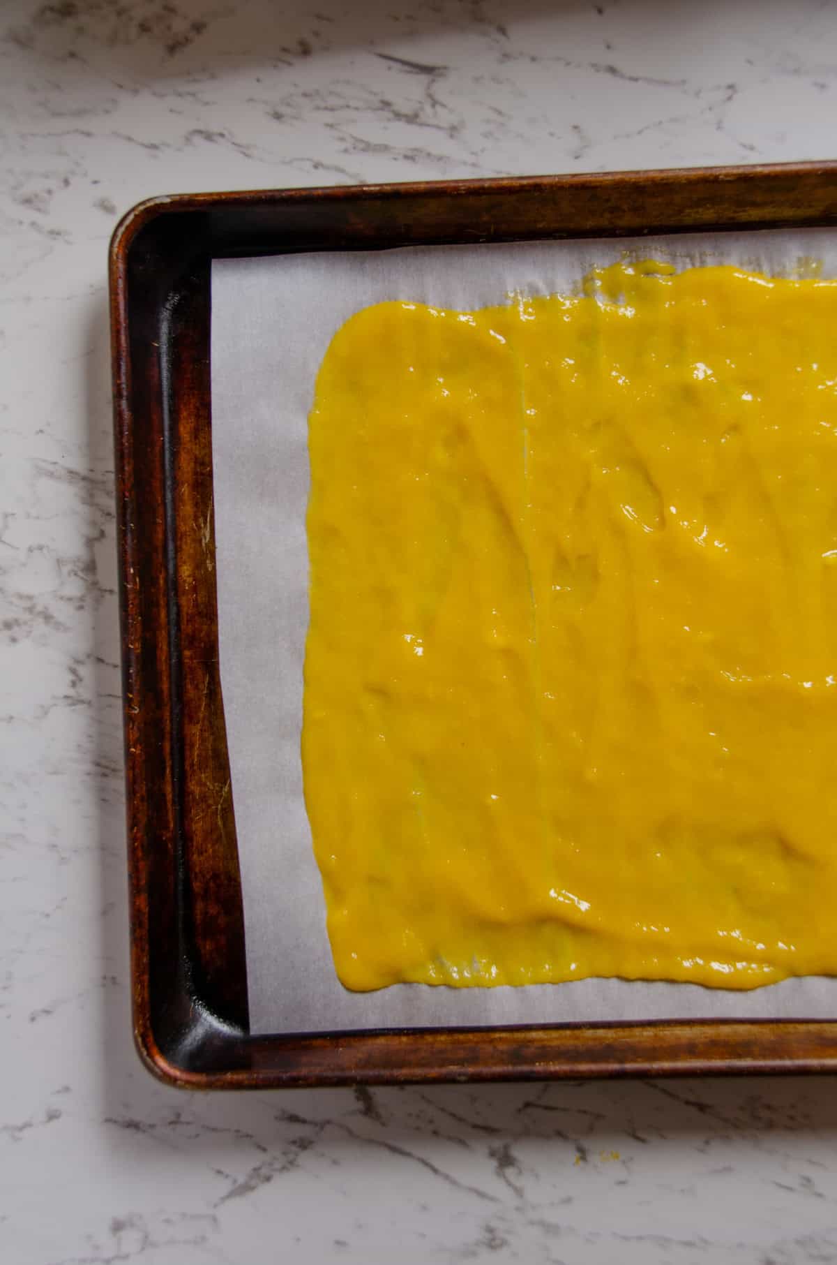 Spreading yellow mango fruit puree on parchment paper.