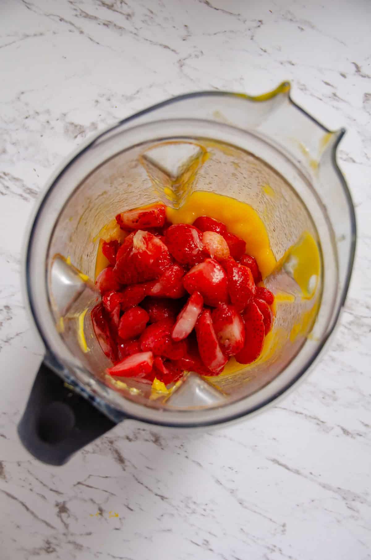 Strawberries in the blender on top of yellow fruit puree.
