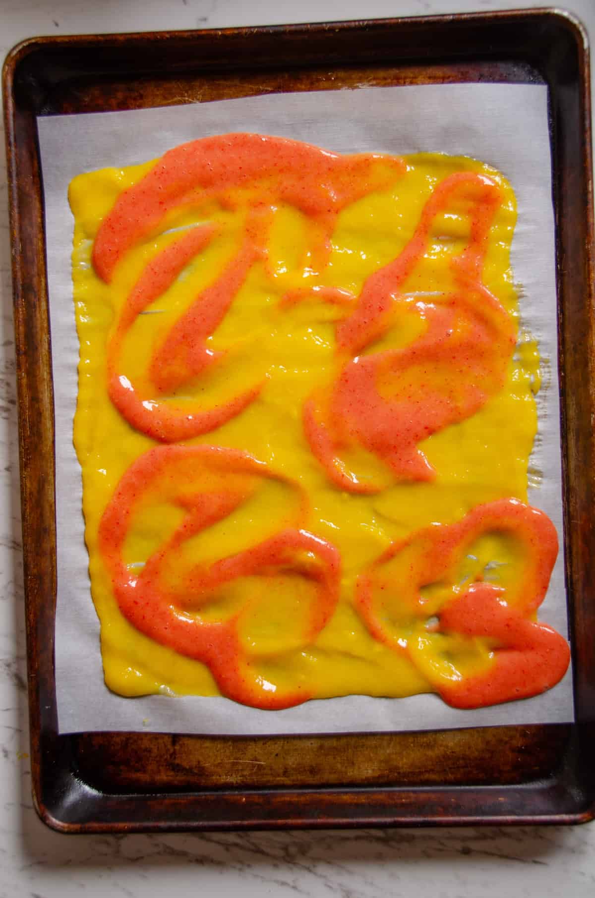 A swirl of pink and yellow fruit puree on parchment paper.