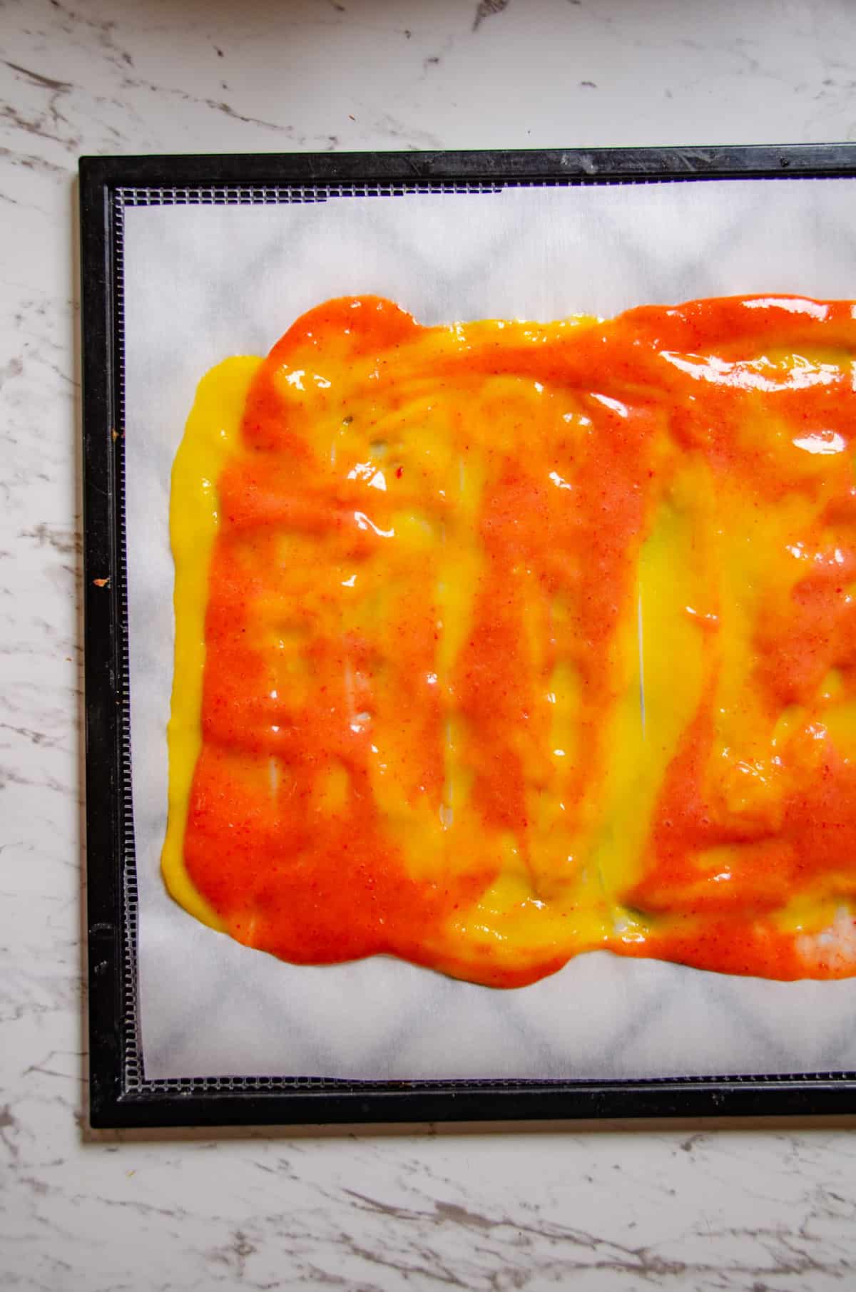 A swirl of pink and yellow fruit puree on parchment paper on dehydrator pan.