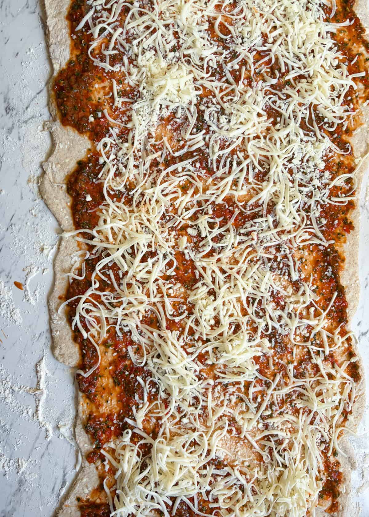 Pizza dough in the counter with red sauce and cheese on top.