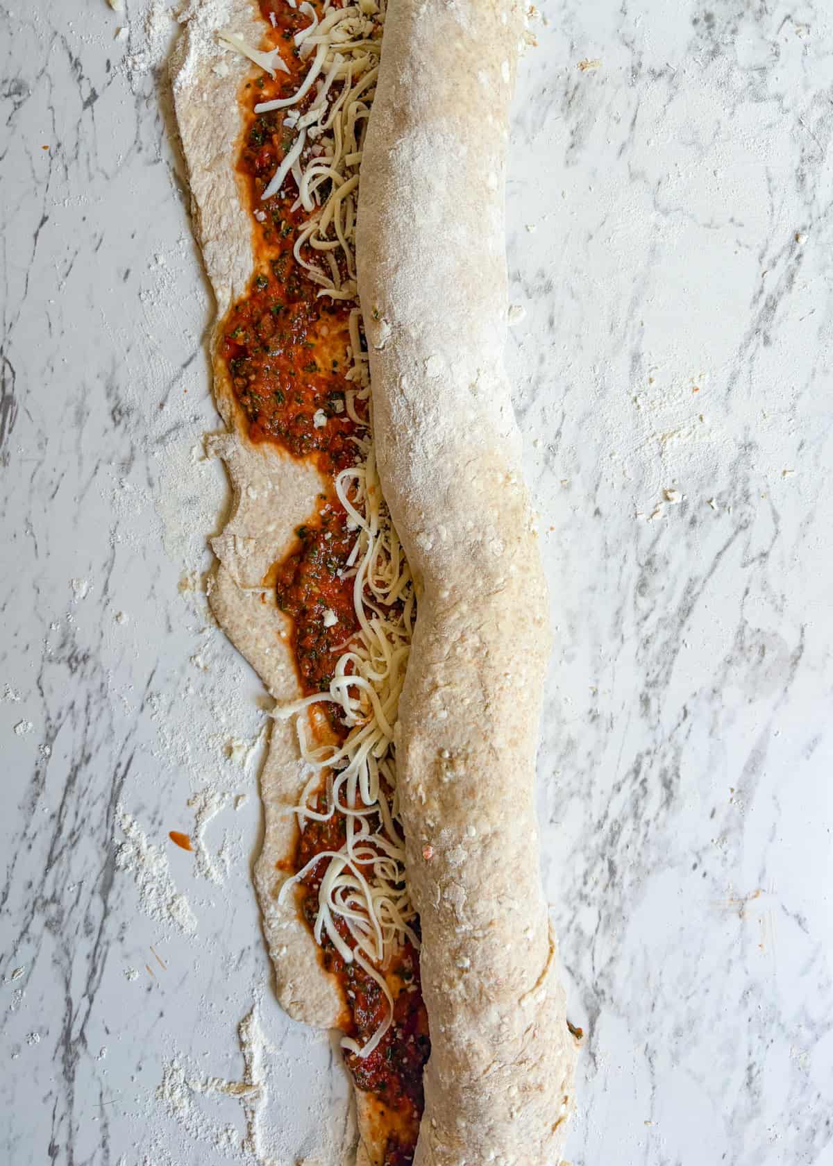 Pizza dough rolled into a log like cinnamon buns with red sauce and cheese on it.