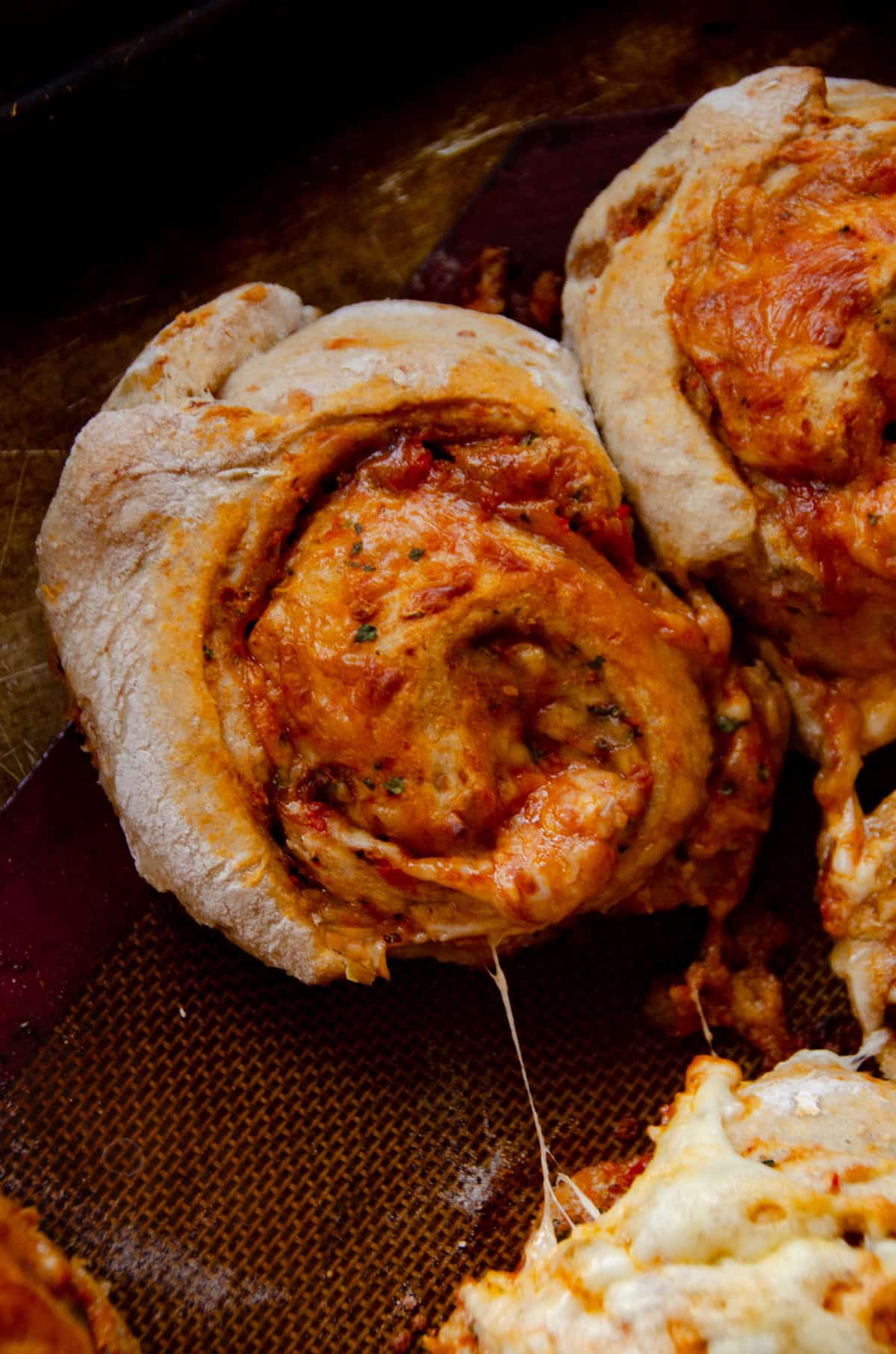 A pizza roll bun with a red sauce in the middle and a string of cheese attached.