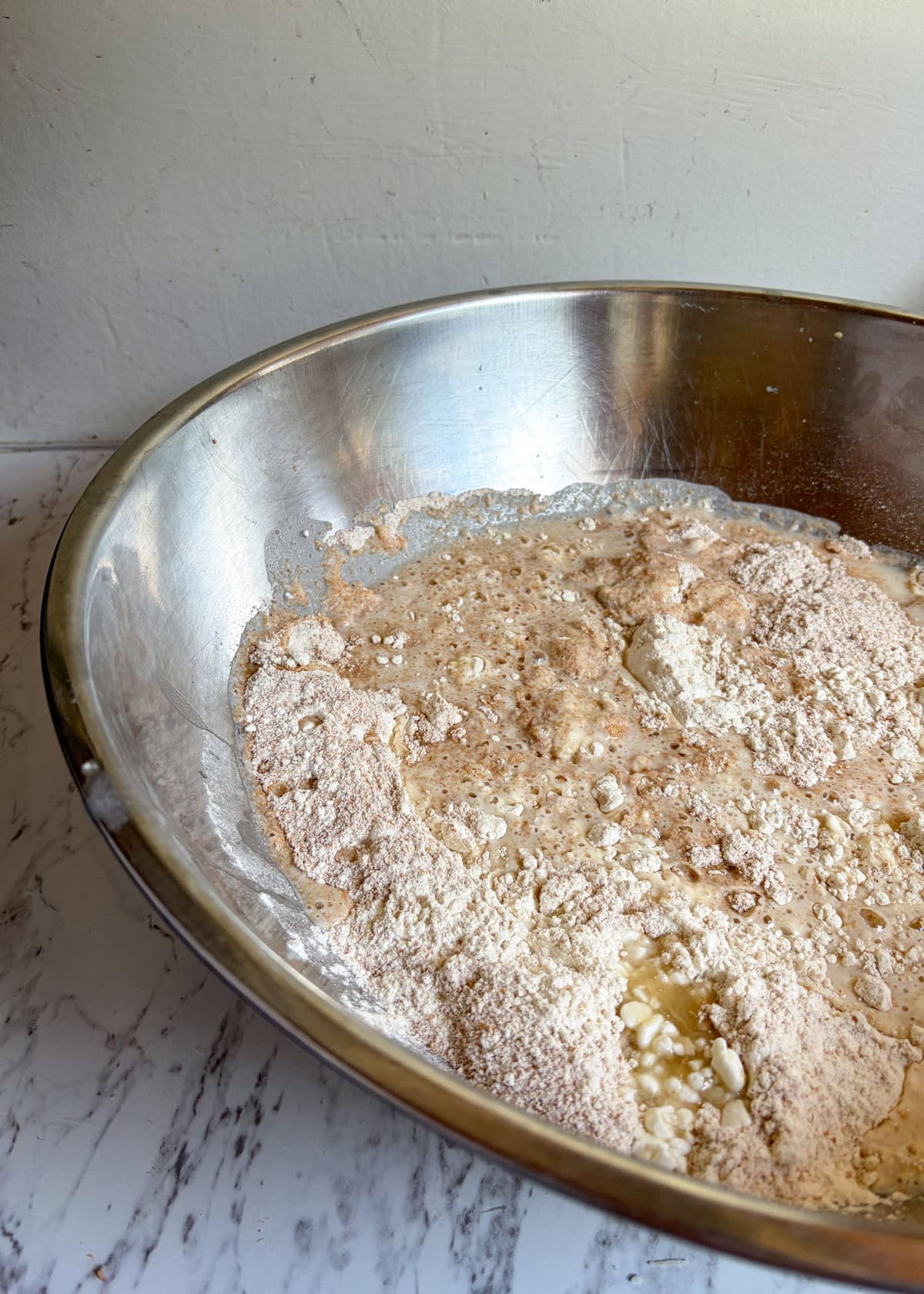 In a large metal bowl is a watery mixture with flour.