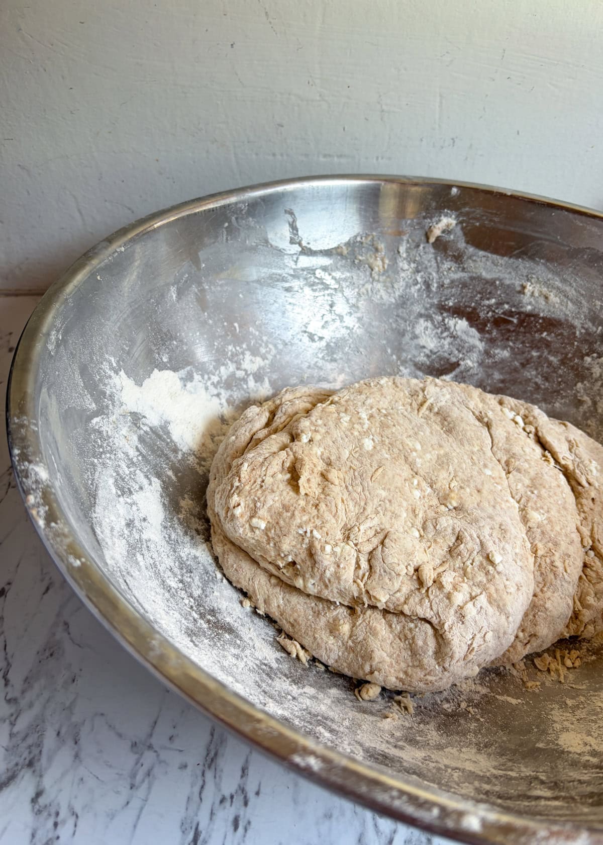 A large metal bowl with pizza dough in it.