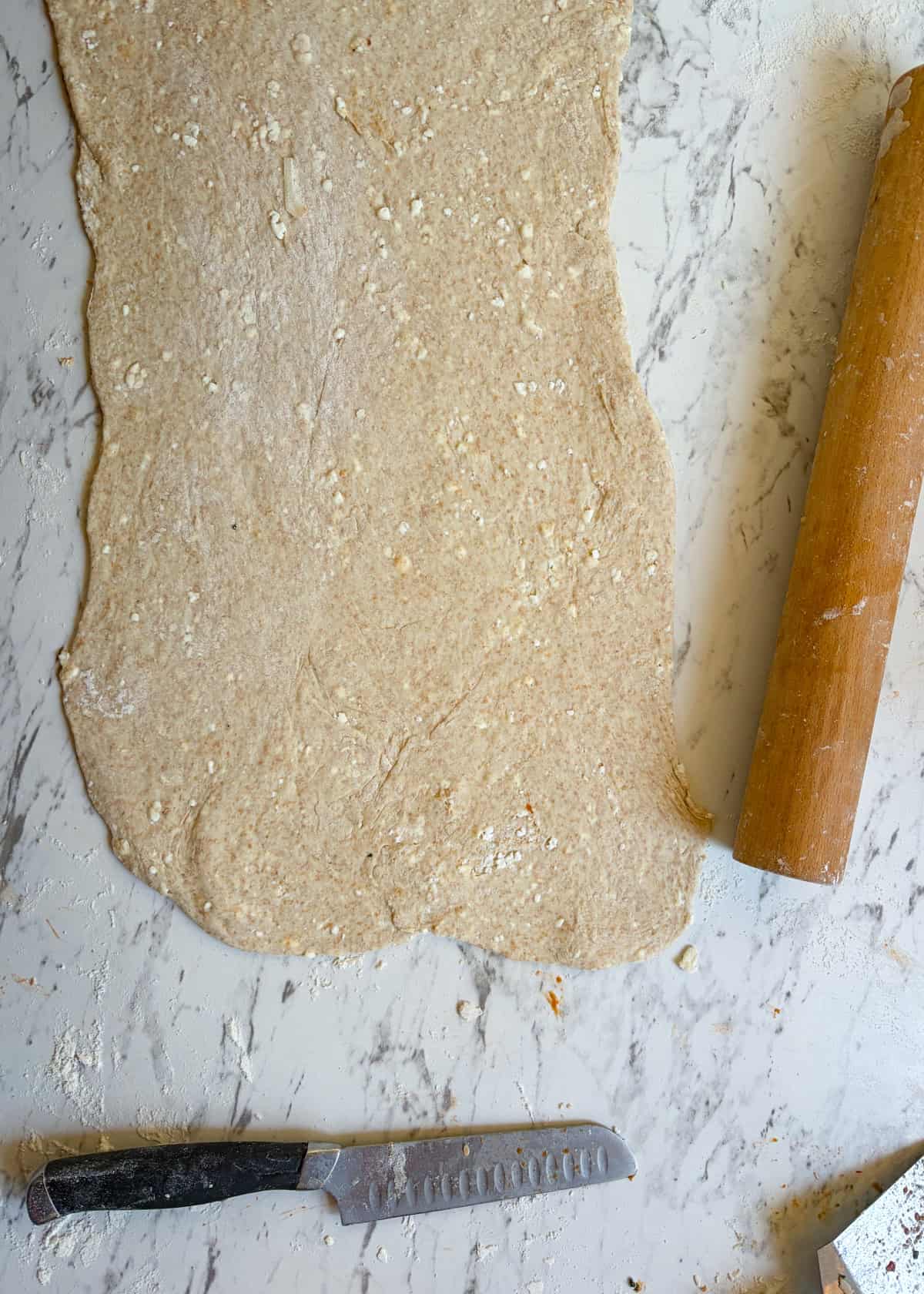 Pizza dough rolled out on the counter with a rolling pin and knife beside it.