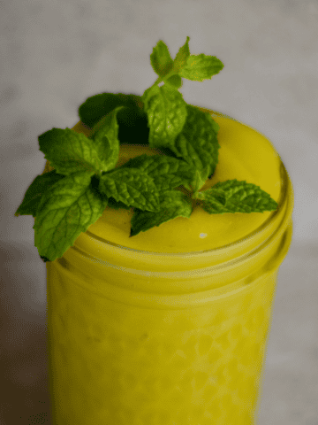 A neon yellow slushie in a jar with fresh mint on top.