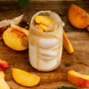 A peach smoothie in a glass cup with yogurt streaks on the inside and peaches all around it.