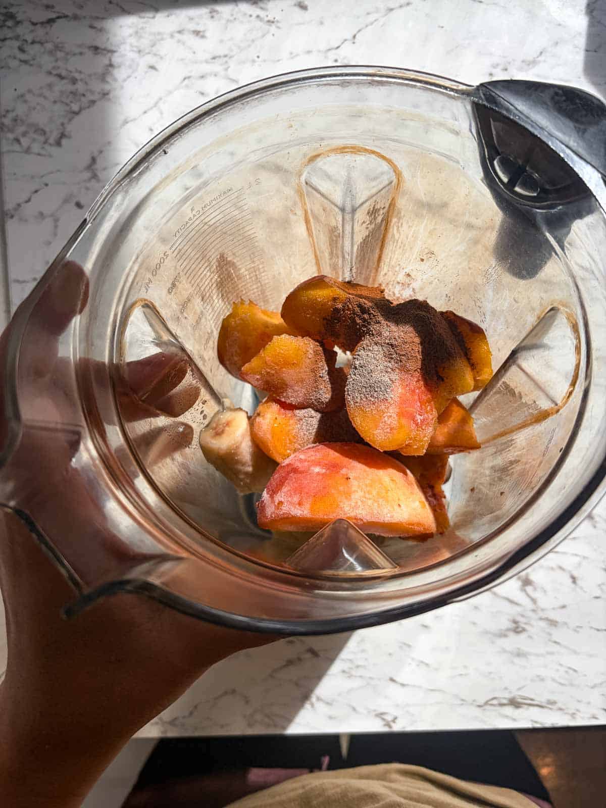 A vitamix container with peaches and spices and milk and banana.
