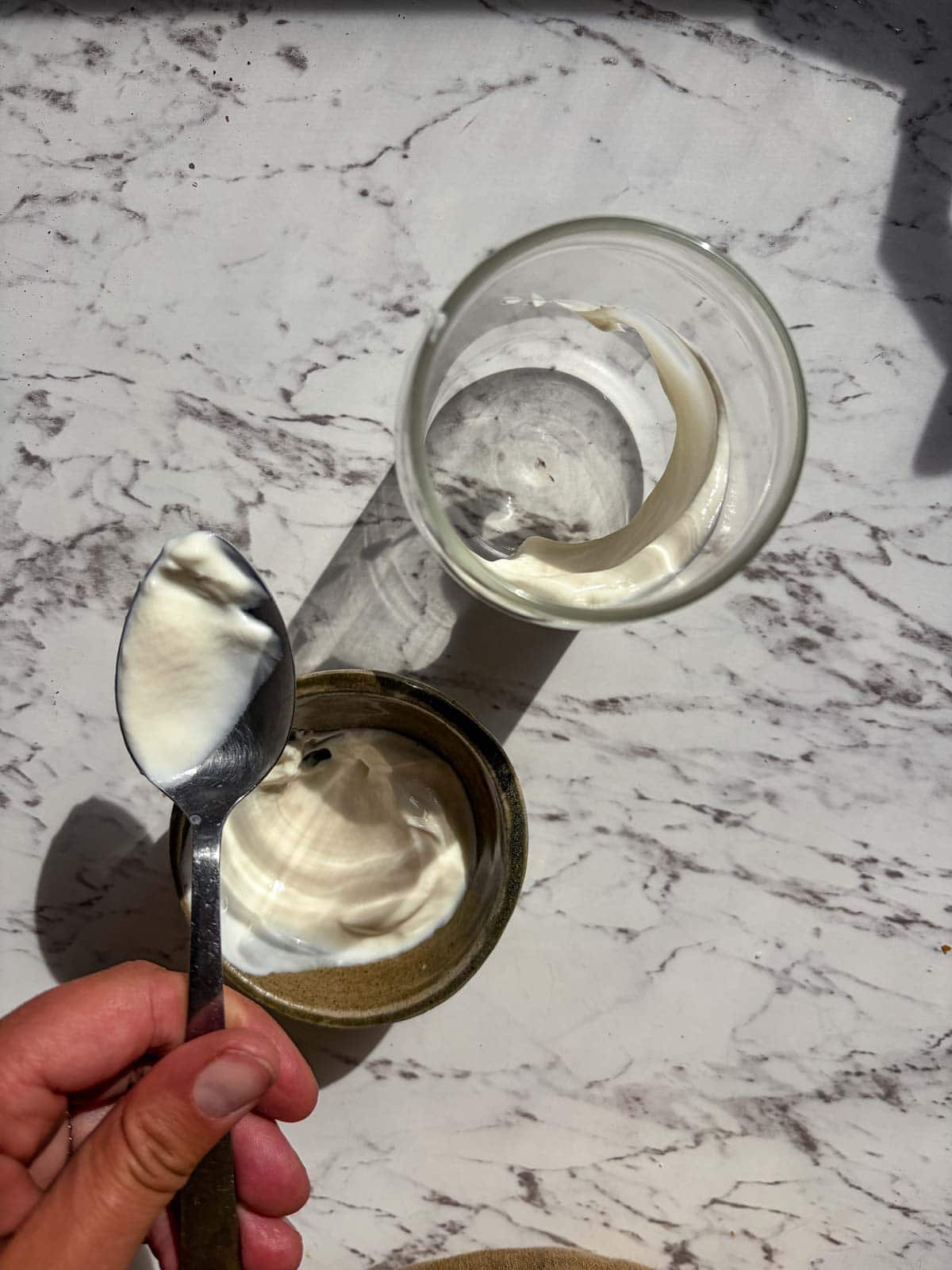 Taking a spoon of yogurt and spreading it on the side of the inside of a glass cup.