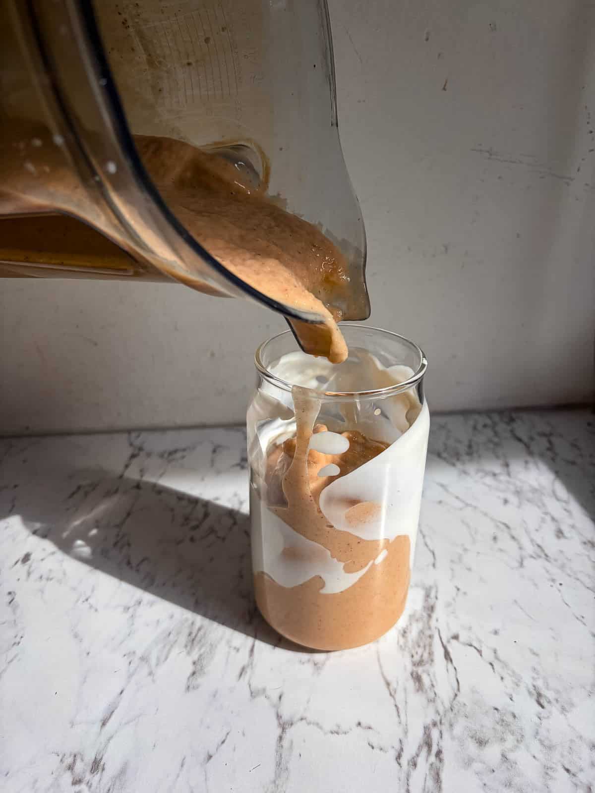 Pouring smoothie into a glass cup with smoothie on the side of it.