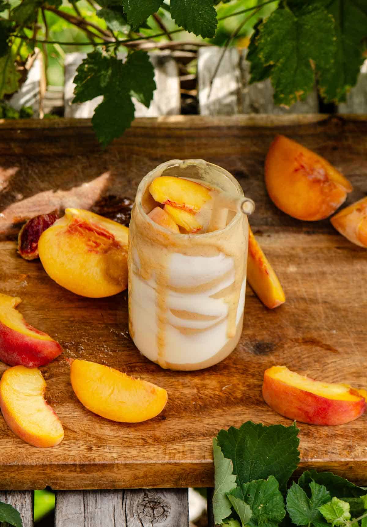 A peach smoothie in a glass cup with yogurt streaks on the inside and peaches all around it.