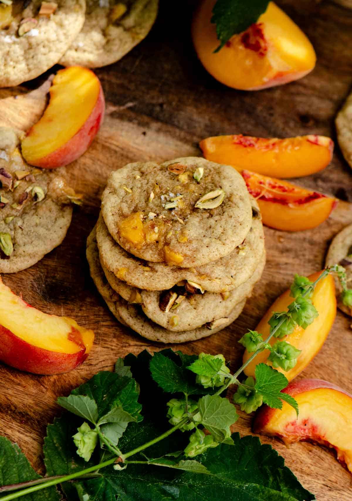 A stack of light brown cookies with a chunk of juicy peach coming out of them with finely chopped pistachios on top.